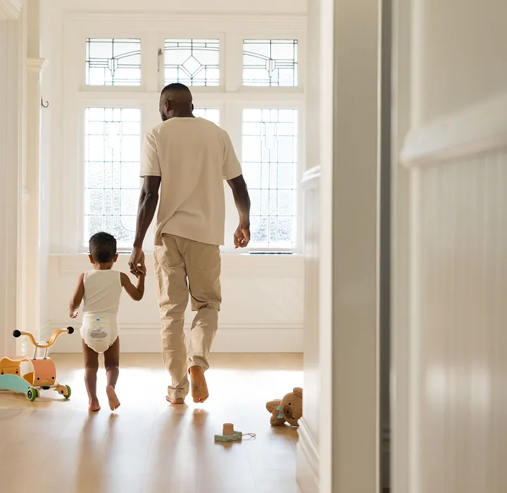 Parent walking hand in hand down a sunlit hallway with a toddler in a Millie Moon diaper