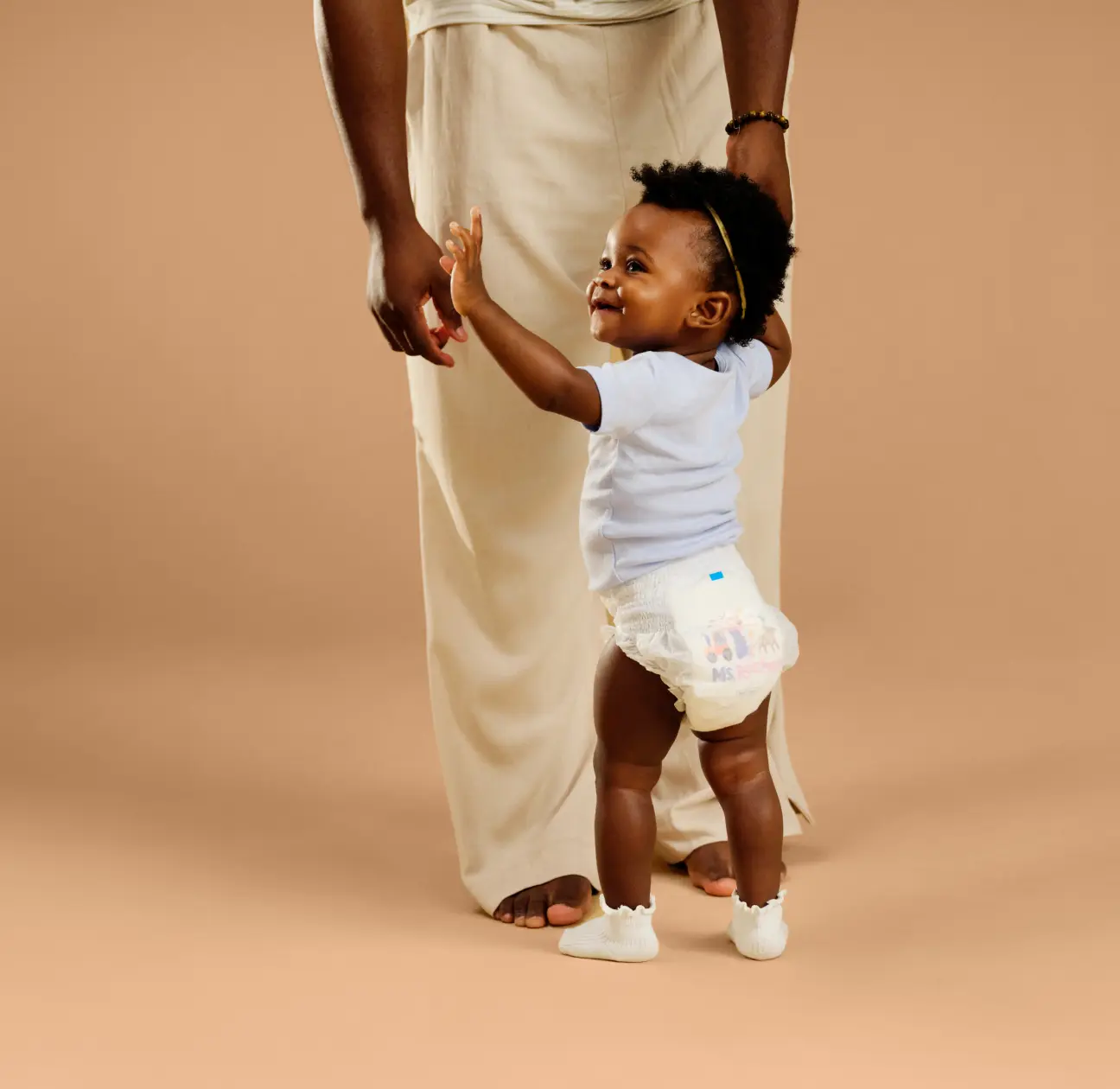 Toddler in Millie Moon Ms. Rachel edition training pants reaching up to hold a parent's hand